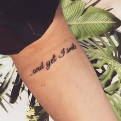 a woman with a tattoo saying and yet i smile on her left arm, next to some tropical leaves