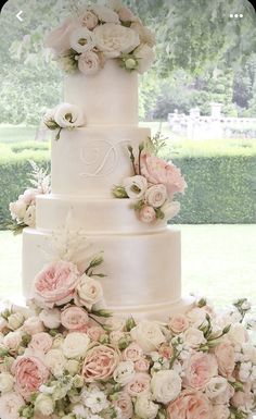 a three tiered wedding cake with pink and white flowers on the bottom, surrounded by greenery