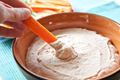 a person dipping dip into a bowl with carrots