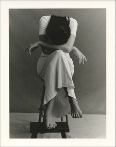 a black and white photo of a woman sitting on a stool with her head in her hands