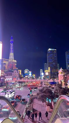 the city is lit up at night with people walking down the sidewalk and cars driving on the street