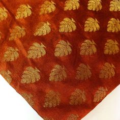 an orange scarf with gold leaf designs on the top and bottom, sitting on a white surface