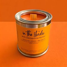 an orange candle with the words in the studio written on it is placed inside a metal tin