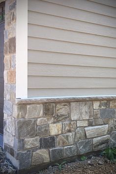 a cat is sitting on the ledge of a stone wall in front of a house