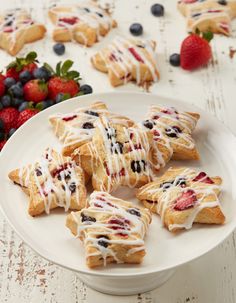 a white plate topped with pastries covered in icing next to berries and strawberries