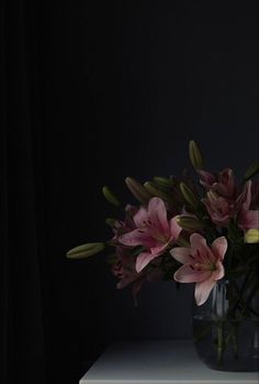 pink flowers in a glass vase on a white table with a black wall behind it