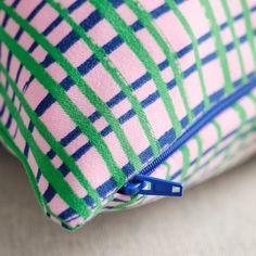 a pink and green plaid pillow with a blue zipper on the bottom that is open