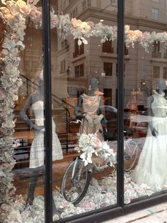 two mannequins dressed in wedding gowns and dresses behind a window display