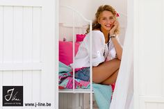 a beautiful woman sitting on top of a bed next to a white door and pink sheets