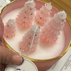 a person is holding a candle with pink flowers on it and the candles are in a bowl