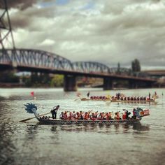 a group of people riding on the back of a boat down a river next to a bridge