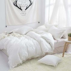 a bed with white comforters and pillows in a room next to a wall hanging