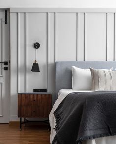 a bedroom with white walls and wood flooring has a gray headboard on the bed