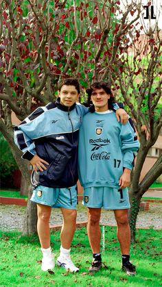 two men standing next to each other in front of a tree