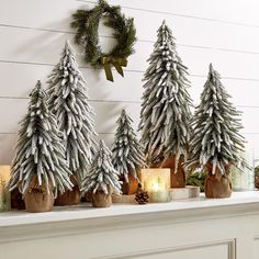 three fake trees are sitting on a mantel with candles in front of them and a wreath hanging from the mantle