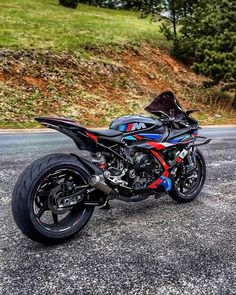 the motorcycle is parked on the side of the road in front of some hills and trees