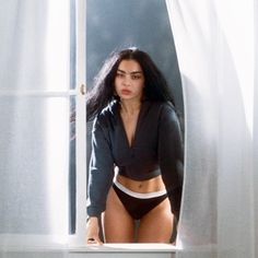 a woman in a black top and panties leaning against a window sill with her hands on her hips