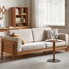 a living room with a white couch and wooden table in front of the window,