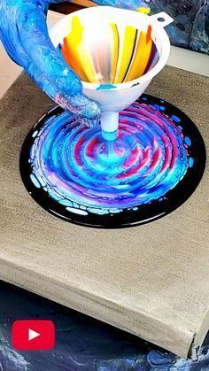 a person is pouring liquid into a bowl on top of a table with blue and red swirls