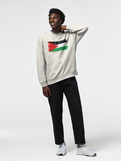 a man in a white sweater and black pants stands with his hands on his head