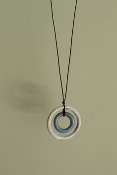 a white and blue necklace hangs from a black cord on a wall with a light green background