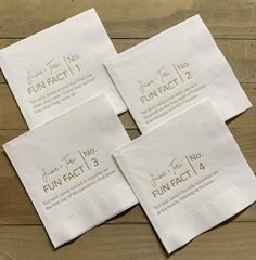 four white napkins with gold foil lettering on them, sitting on top of a wooden table