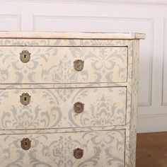 an old white dresser with ornate designs on it's drawers and knobs, in front of a wall