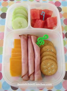 a plastic container filled with fruit, crackers and meats on top of a polka dot table cloth