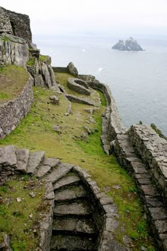 stairs lead down to the ocean from an old stone wall with moss growing on it