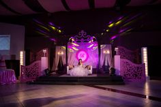 a bride and groom are sitting on the stage at their wedding reception with purple lighting