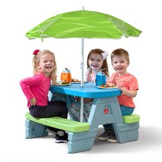 three children sitting at a table under an umbrella