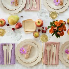 the table is set with plates, silverware, and fruit on it's surface