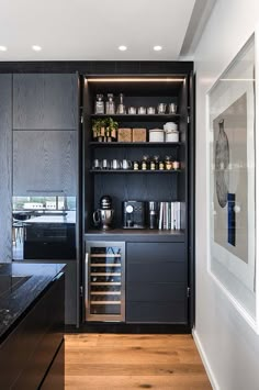 a kitchen with black cabinetry and wooden flooring in the center is lit by recessed lights