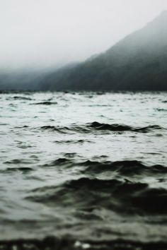 a black and white photo of the ocean with mountains in the backgroung