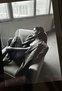 a black and white photo of a man laying on a couch in front of a window