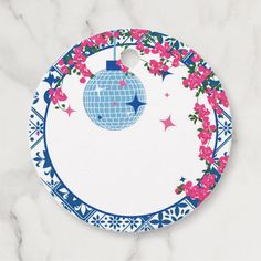 a blue and white christmas ornament with pink flowers around it on a marble surface