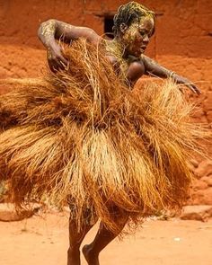 a woman is dancing in the dirt with grass on her head and arms, while wearing a skirt