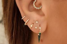 a woman wearing three different ear piercings with green and white stones on the sides