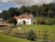 a large white house sitting in the middle of a lush green field next to a forest