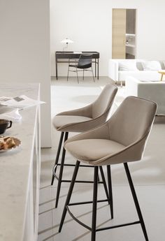 three modern bar stools in the middle of a room with white walls and flooring