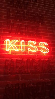 a red neon sign that says kiss and drink on the side of a brick wall