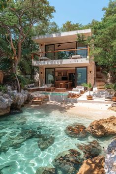 the house is surrounded by trees and rocks, with clear blue water running through it