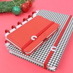 a red notebook sitting on top of a black and white checkered binder next to a christmas ornament