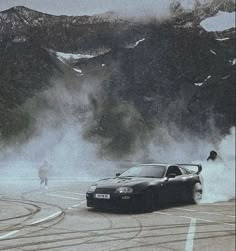 a black sports car driving down a road next to snow covered mountains and people in the distance