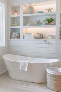 a white bath tub sitting under a window next to a shelf filled with sea shells