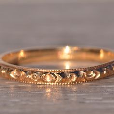 a close up of a gold wedding ring on a wooden surface with light shining in the background