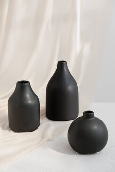 three black vases sitting next to each other on a white cloth covered tablecloth