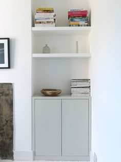 a white shelf with books on top of it next to a wall mounted clock and pictures