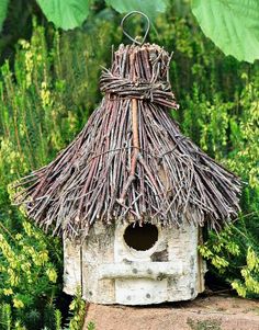 a birdhouse made out of sticks and grass with flowers in the backgroud