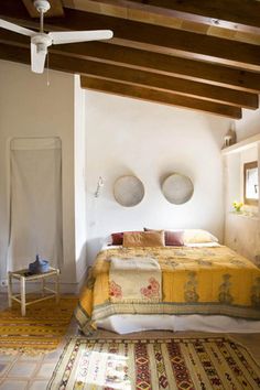 a bed sitting in a bedroom next to a ceiling fan and rug on top of a wooden floor